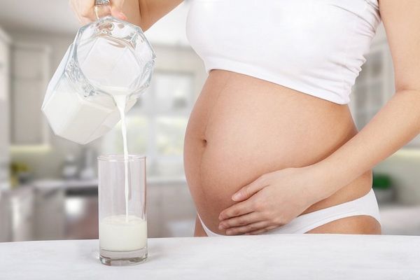 Беременная девушка наливает в стакан молоко